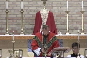 Pastor Brent Bowman står med bøjet hoved under den eukaristiske bøn ved en skolemesse i St. Gabriel the Archangel Catholic Church.