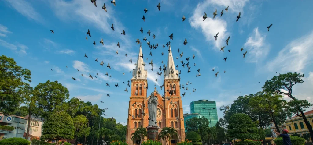 Flock av fugler som flyr over Notre-Dame-katedralen i Saigon i livlig dagslys.