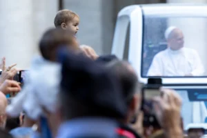 Et barn løftes op mod pave Leo XIV, der passerer i pavemobilen på Peterspladsen.