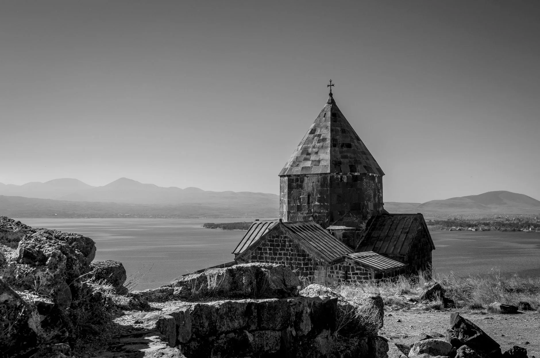 Et rolig monokromatisk bilde av et historisk kapell ved innsjøen Sevan, Armenia, blant fjell og rolige farvann.